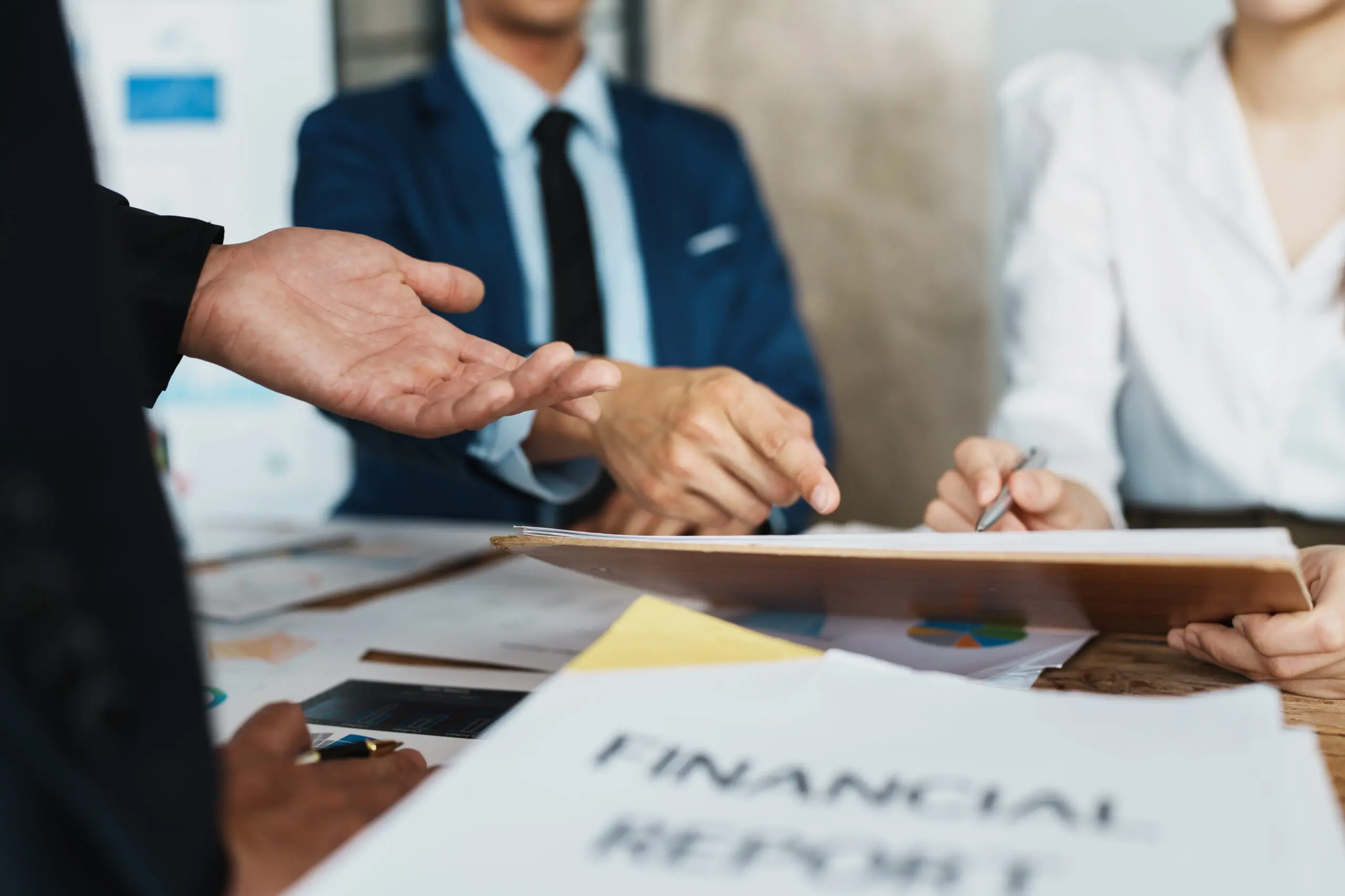 Professionals discussing over a document labeled "FINANCIAL REPORTS" at a business meeting.